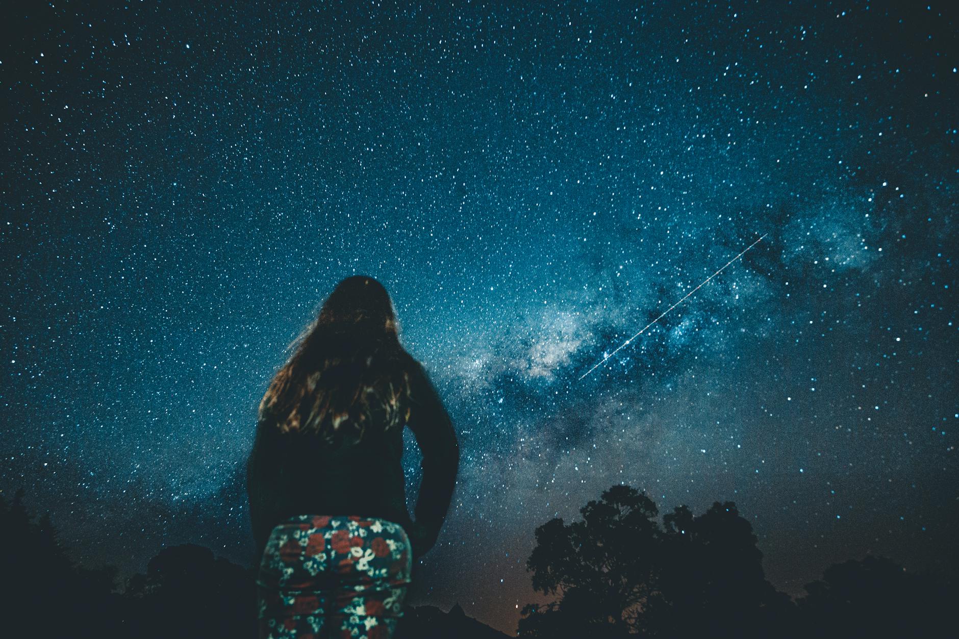 Woman with arms wide open under a vast starry sky representing the expansion and joy of the 1313 angel number