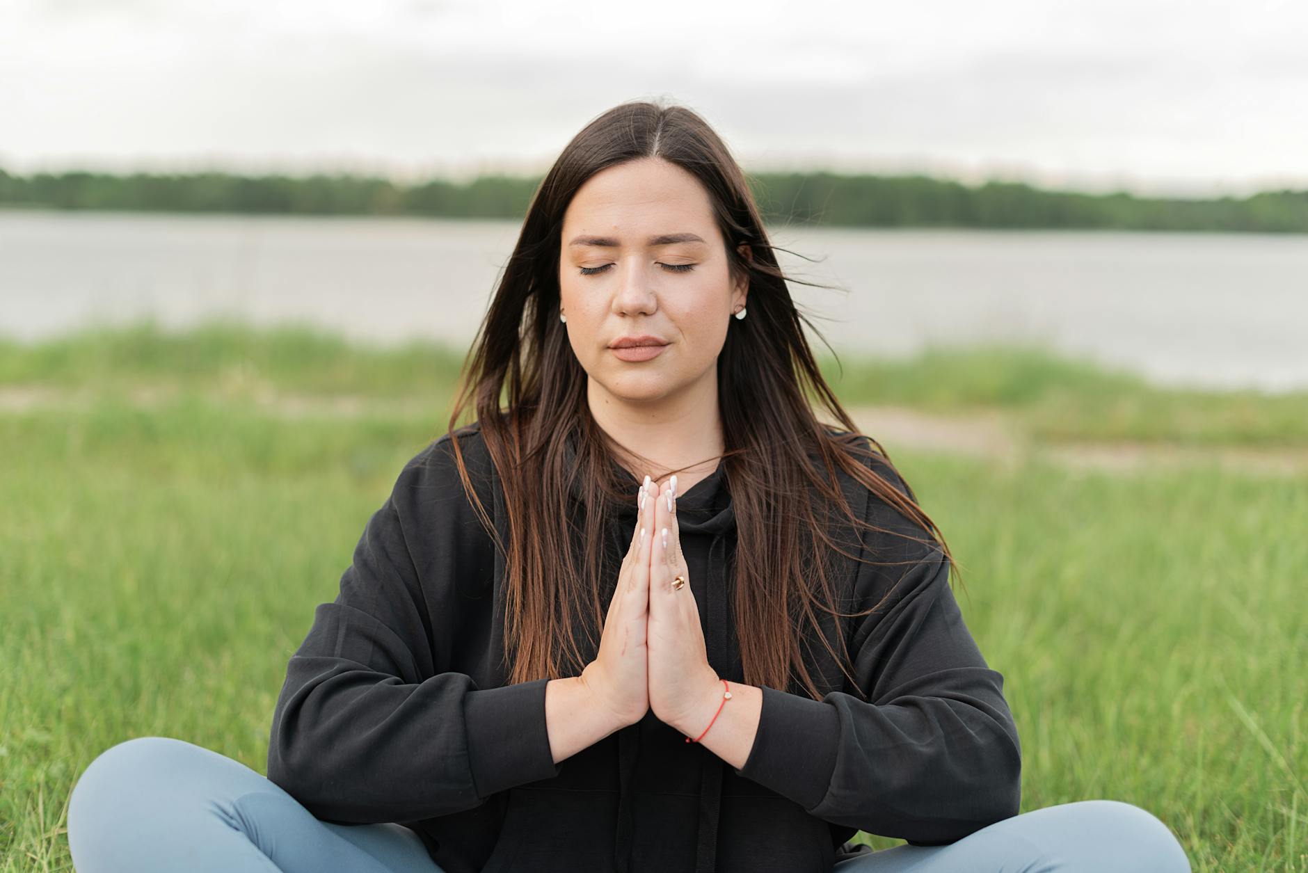 Woman in meditative stillness by water at dusk representing the transformative trust and divine potential energy of the 2020 angel number